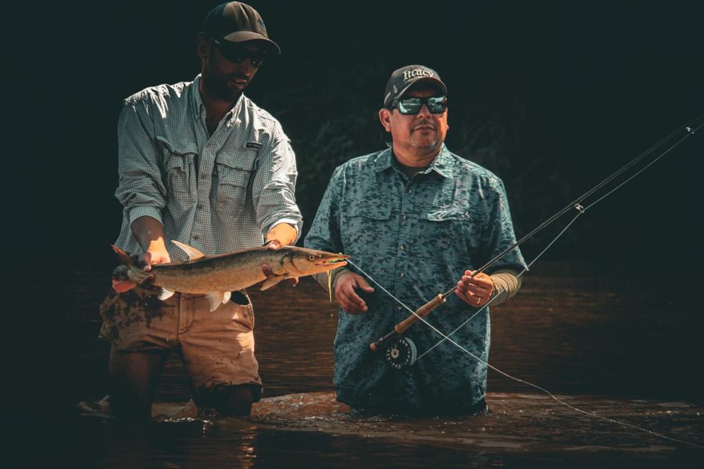 A guide holding a bicuda while an angler stands beside him with a fly rod