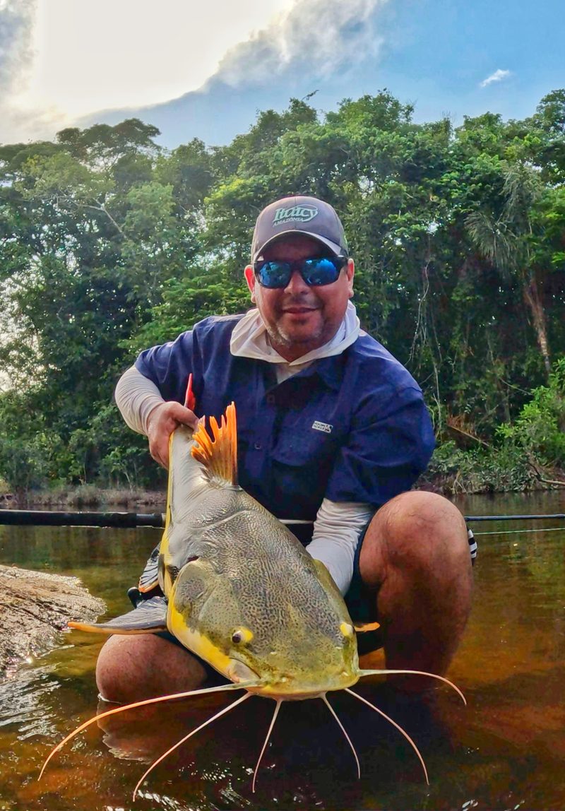 Rodrygo holding a redtail catfish (pirarara) in shallow water